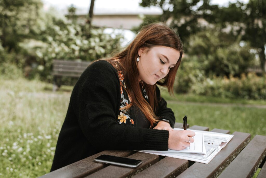 Woman writing notes in papers in park.