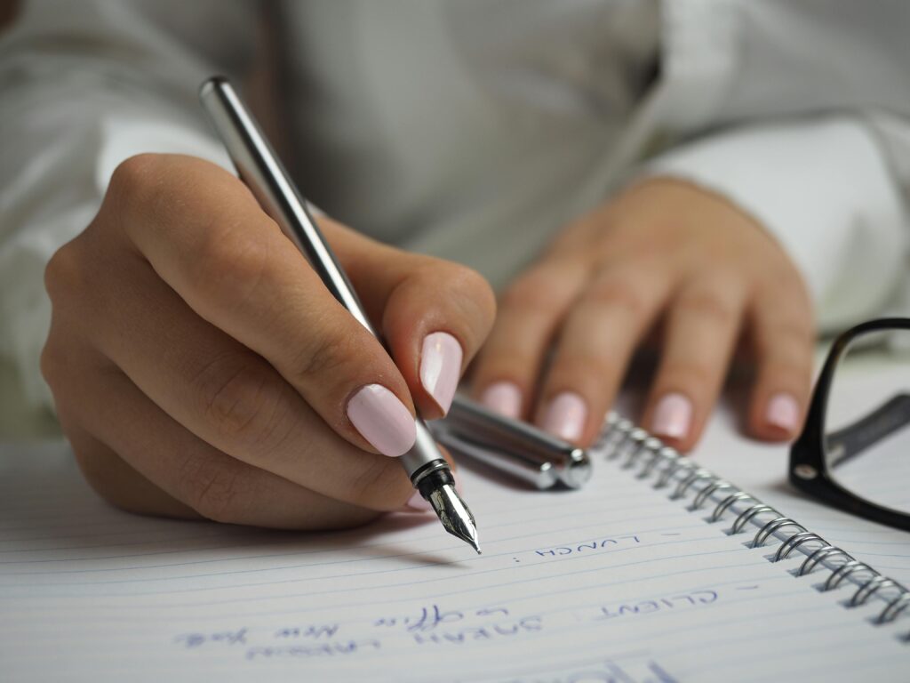 Woman in white long sleeved shirt holding a pen writing on a paper.